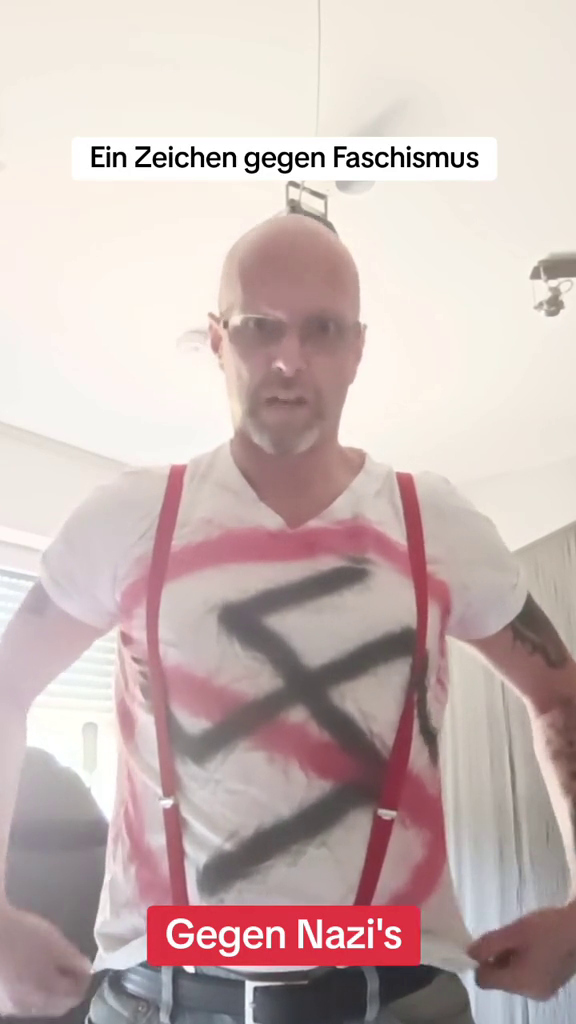 Stephan M. trägt ein weißes T-Shirt, auf das ein durchgestrichenes Hakenkreuz gesprüht wurde. Darüber Text: "Ein Zeichen gegen Faschismus" und "Gegen Nazi's"
