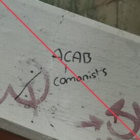 In schwarzem Marker geschriebener Schriftzug "ACAB" mit einer Linie, die von dem C auf das Wort "comonists" weist, neben einem durchgestrichenen Hammer und Sichel-Symbol, an einem Betonteil eines Treppenaufganges.