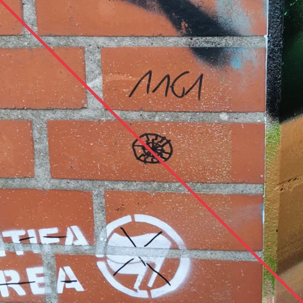 Eine Schwarze Sonne und der Schriftzug "1161" in schwarzem Marker und ein durchgestrichenes Graffiti "Antifa Area", an einer Mauerwand.