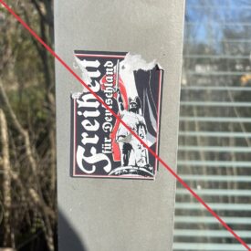 Aufkleber mit Aufschrift "Freiheit für Deutschland", einer Reichsflagge und einer Zeichnung des Hermannsdenkmals auf dem Rahmen eines Wartehäuschens.