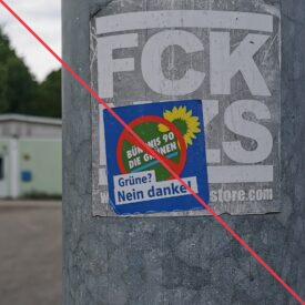 Aufkleber mit Aufschrift "Grüne? Nein danke!" und einem durchgestrichenen Logo von Bündnis 90/Die Grünen, der einen "FCK NZS"-Aufkleber überdeckt.