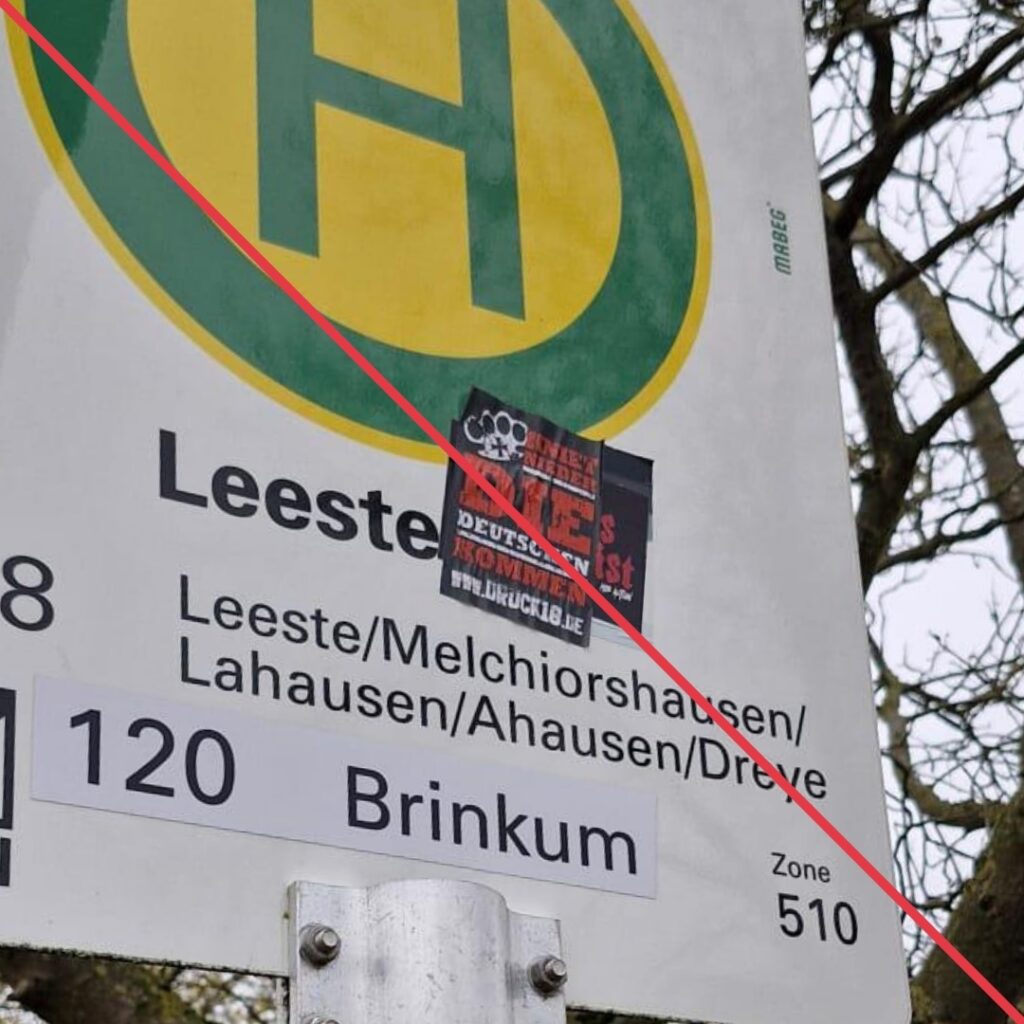 Aufkleber mit Aufschrift "Kniet nieder, die Deutschen kommen" und Werbung für einen neonazistischen Versandhandel auf einem Bushaltestellenschild.