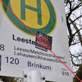 Aufkleber mit Aufschrift "Kniet nieder, die Deutschen kommen" und Werbung für einen neonazistischen Versandhandel auf einem Bushaltestellenschild.